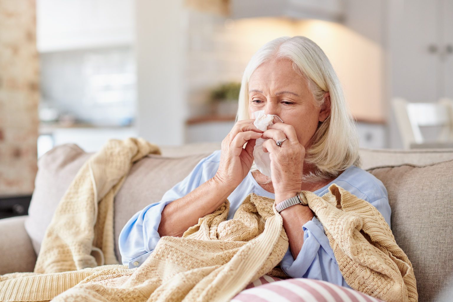 Shot of a senior woman blowing her nose while feeling sick at home.