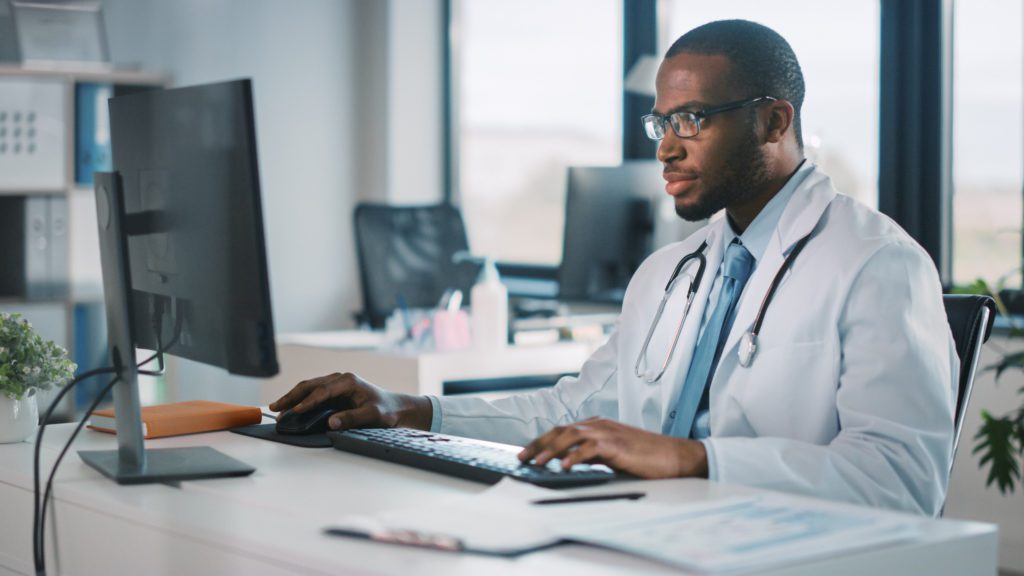 Candid image of a doctor wearing glasses looking pensively in his computer.