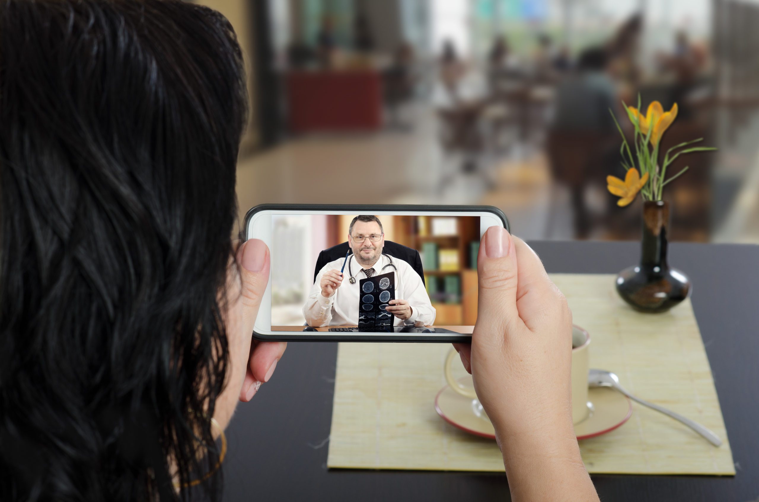 Image of a woman in a restaurant holding a phone during virtual consultation.